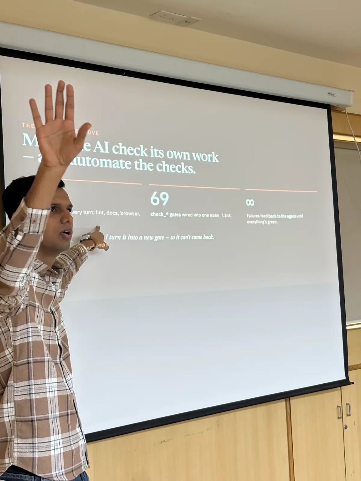 Gaurav raises his hand while pointing at a presentation slide about AI checks and gates.
