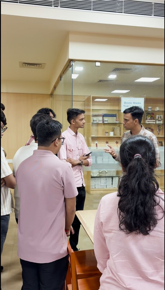 A small group talks near a glass display case labeled Book Mark in a library area.